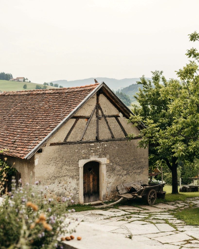 Kleines steirisches Steinhaus mit Holzgiebeldach, herzförmigem Türschnitt und Holzwagen
