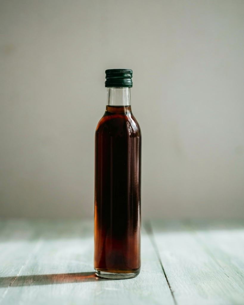 Klare Glasflasche mit dunklem steirischem Kürbiskernöl auf hellem Holz