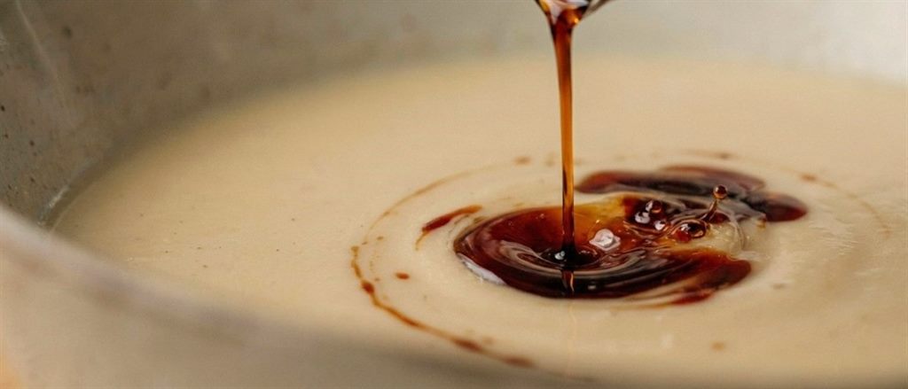 Dünner Strahl dunklen Kürbiskernöls fließt auf cremige Suppe
